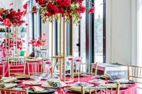a chic and bold wedding tablescape with a tall floral centerpiece, red linens, gold chargers and cutlery