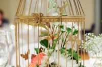 a chic golden cage with white and coral blooms and greenery is a creative alternative to a usual arrangement