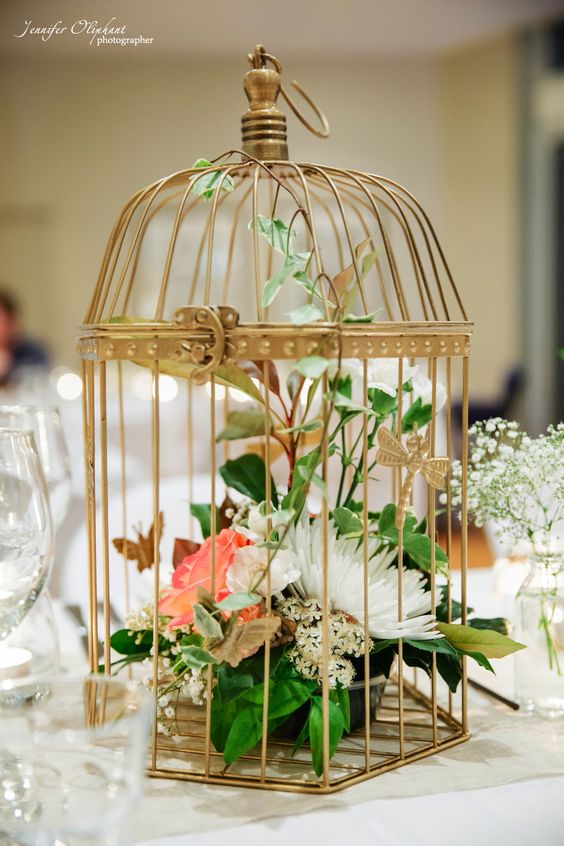 a chic golden cage with white and coral blooms and greenery is a creative alternative to a usual arrangement