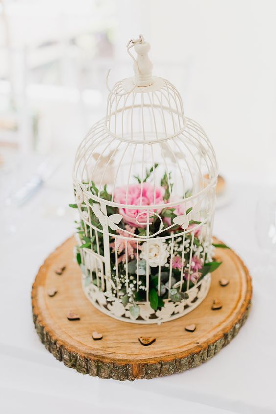 a chic rustic wedding centerpiece of a tree slice and a white cage with white and pink blooms and greenery