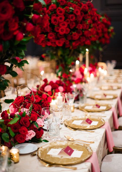 a chic wedding tablescape with red and pink roses, gold chargers, gold cutlery and candleholders plus some glasses