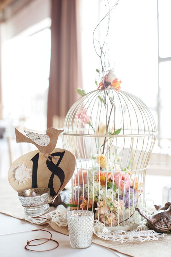 a cluster wedding centerpiece of a cage with pastel blooms and candles around it is a cool idea