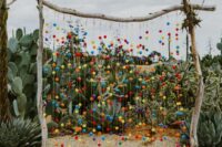 a colorful Mexican wedding backdrop with bright pompoms and tassels, a bright striped rug is a cool idea for a boho wedding