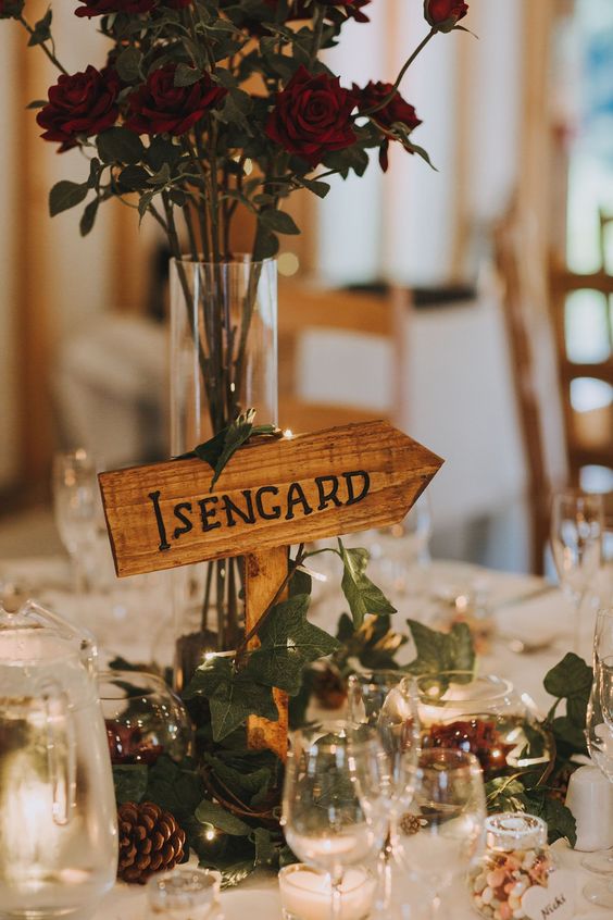 a cool LOTR wedding centerpiece of red roses, vines, pinecones, lights and an Isengard sign and candles around