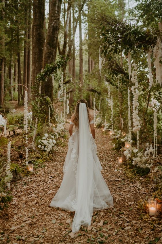 a dreamy forest wedding aisle with white blooms, greenery and candles will fit a LOTR wedding