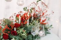 a fantastic Christmas wedding tablescape with an evergreen and red rose and berry runner, gold chargers and cutlery