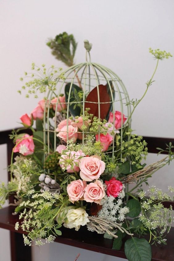a fantastic wedding centerpiece of a green cage with pink and coral blooms and lots of greenery