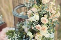a gorgeous cage decorated with crystals, blush and white blooms and greenery as a refined wedding centerpiece