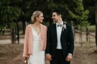 a lace wedding dress with a V-neckline and a pink cardigan on top are a cool and romantic combo for a wedding