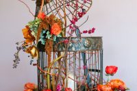 a large cage with a pillar candle, bold ornage and red blooms, greenery and twigs is wow