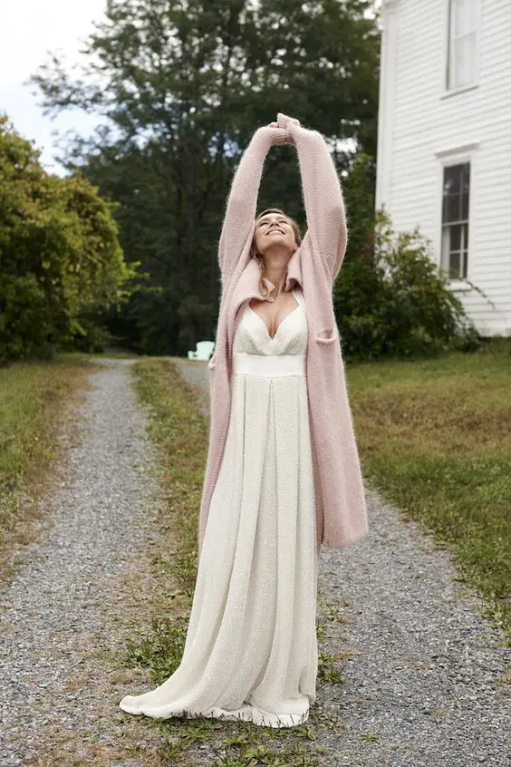 a long blush cardigan paired with a simple and romantic wedding dress with a sweetheart neckline and a pleated skirt