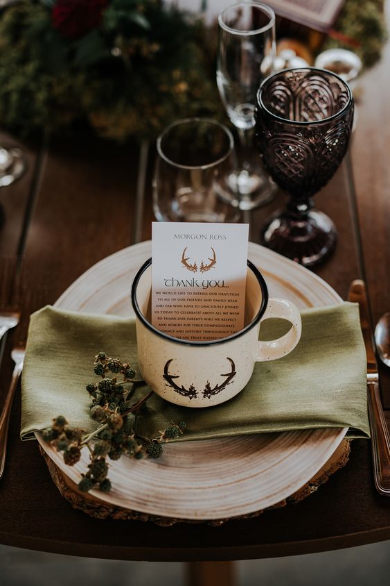 a lovely magical place setting with a tree slice as a placemat, a plate, a mug, some greenery and dark glasses