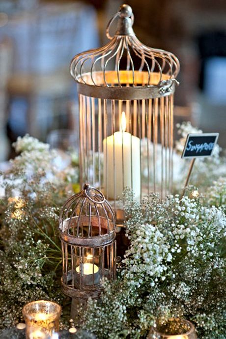 a lovely wedding centerpiece of baby's breath, cages as candleholders and a chalkboard sign