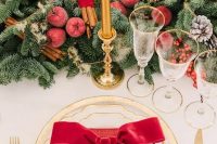 a luxurious Christmas wedding tablescape with an evergreen runner, sugared apples, berries and cinnamon sticks, gold rim plates and red napkins