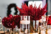 a luxurious wedding centerpiece of red blooms in gold vases, pillar and floating candles and gold chargers and cutlery