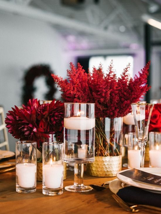 a luxurious wedding centerpiece of red blooms in gold vases, pillar and floating candles and gold chargers and cutlery