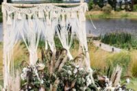 a macrame and tassel wedding backdrop with lots of greeneyr, white blooms and king proteas plus a rug is a great idea for a boho wedding