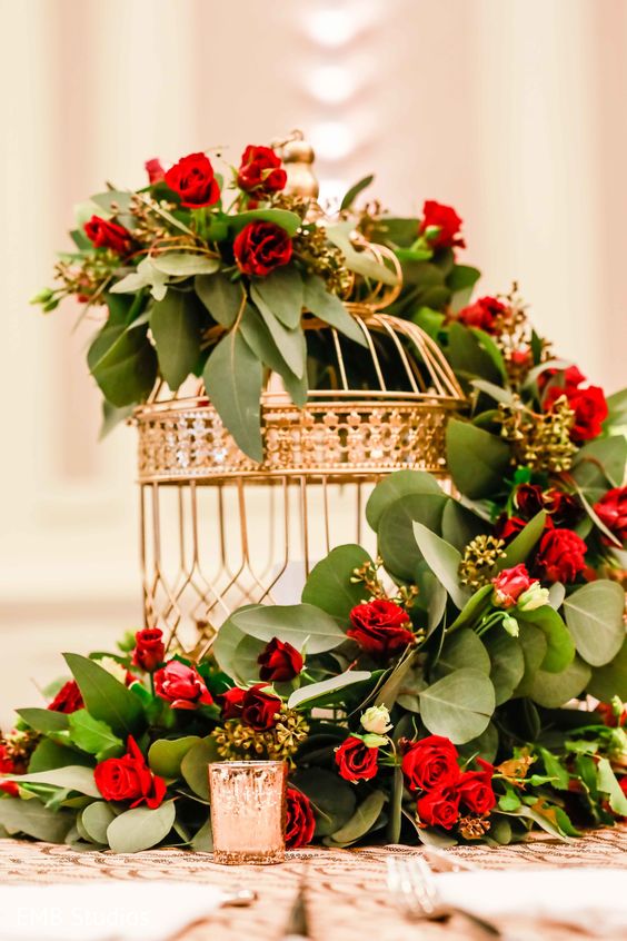 a magical wedding centerpiece of a gold cage with a candle, greenery and red roses is a chic and catchy idea
