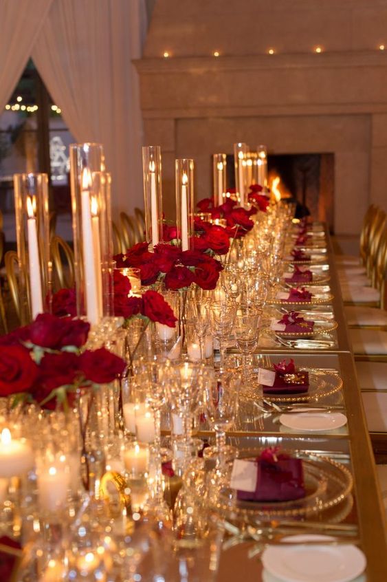 a modern and refined wedding tablescape with pillar candles, red roses, clear plates with a gold rim and gold cutlery