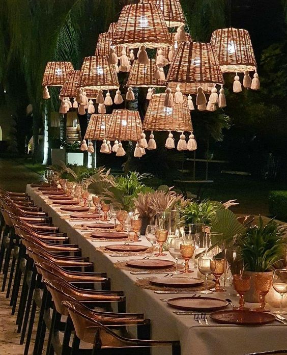 a neutral boho wedding reception space with woven lamps with tassels, greenery and dried fronds, amber glasses and terracotta chargers