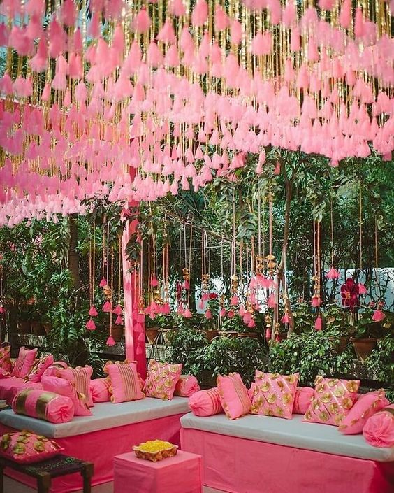 a pink wedding lounge with pink pillows, ombre pink tassels over the space is a great idea for a wedding, it looks bold and elegant
