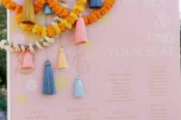 a pink wedding seating chart with colorful tassels, bright flower garlands is a nice idea for a colorful and fun wedding