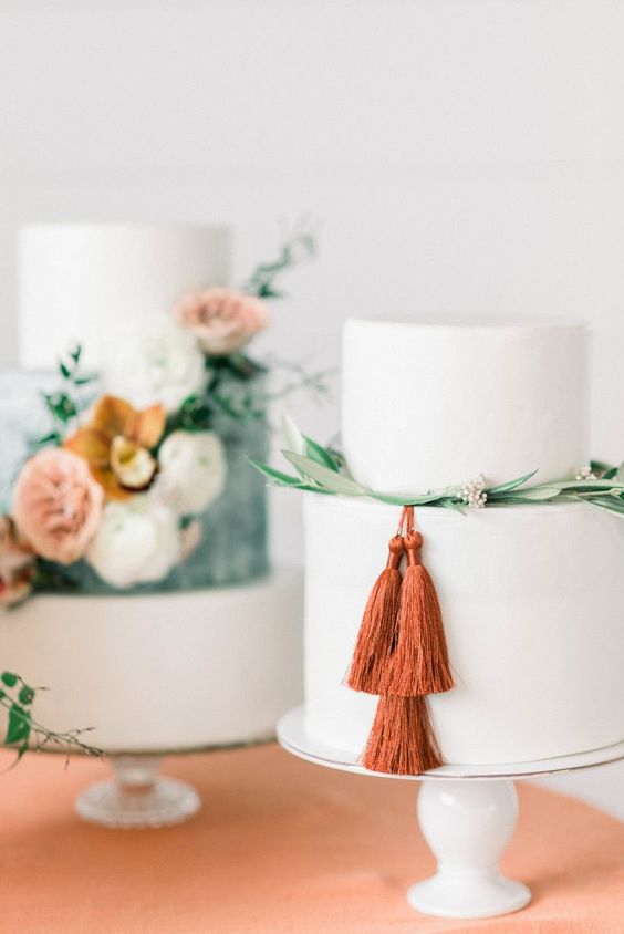 a plain white wedding cake decorated with greenery and berries and rust-colored tassels is a lovely idea for a bold modern wedding