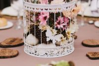a pretty woodland wedding centerpiece of a cage with pink and white blooms, rocks and pinecones