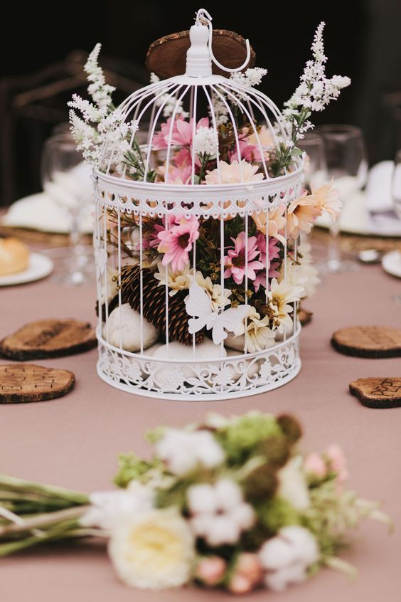 a pretty woodland wedding centerpiece of a cage with pink and white blooms, rocks and pinecones