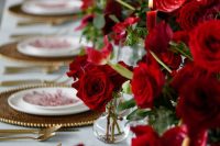 a refined wedding table setting with gold chargers and cutlery, bold red floral centerpiece and red candles is amazing