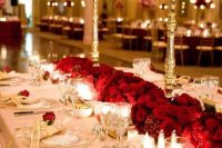 a refined wedding tablescape done with red roses on stands and on the table, gold touches and a blush tablecloth for more elegance