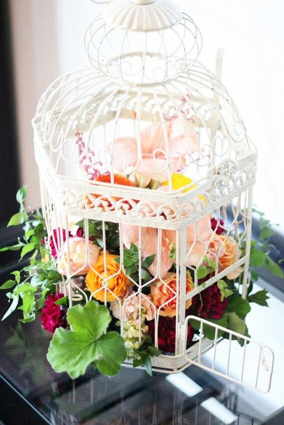 a refined white cage with pink, yellow and burgundy blooms and greenery as a catchy wedding centerpiece