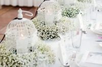 a row of small white cages with pilalr candles and baby’s breath is a lovely wedding centerpiece idea