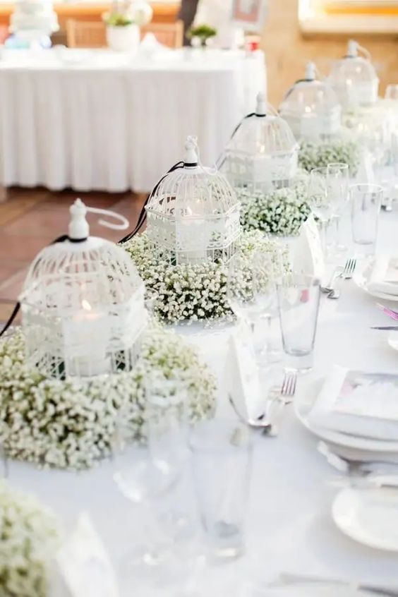 a row of small white cages with pilalr candles and baby's breath is a lovely wedding centerpiece idea