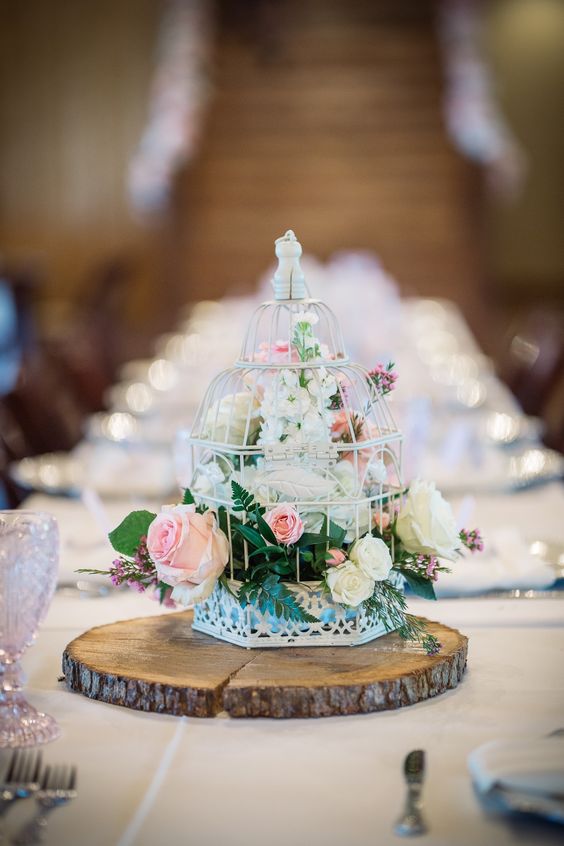 a rustic wedding centerpiece of a tree slice, a white cage with white and blush blooms and greenery