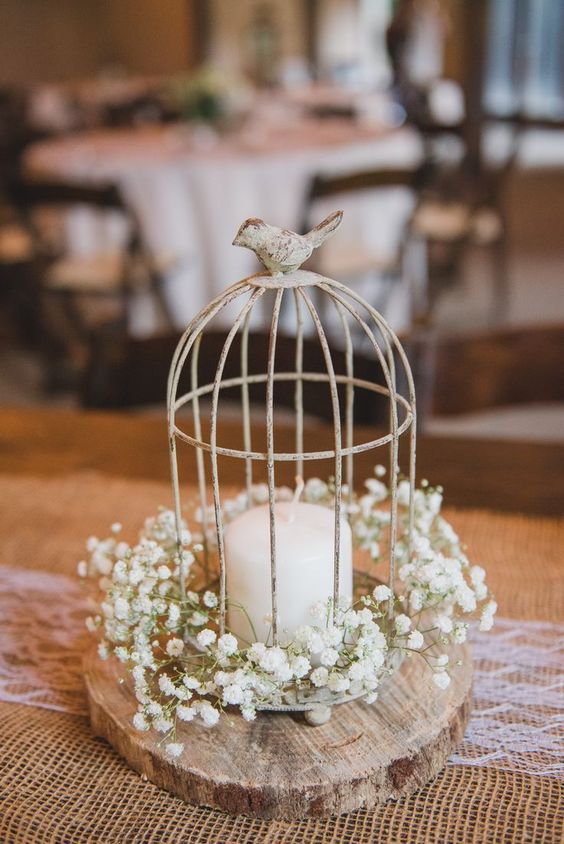 a rustic wedding centerpiece of a tree slice, baby's breath, a cage with a candle is a lovely and cute idea