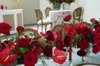 a sophisticated wedding tablescape with lush red florals, red candles, gold placemats and gold cutlery is chic