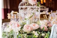 a vintage wedding centerpiece of a white cage with a candle, blush peony roses and greenery is amazing