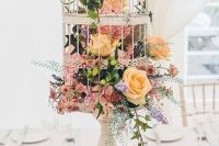 a vintage white cage placed on a stand with muted blooms and greenery is a chic idea for a vintage wedding