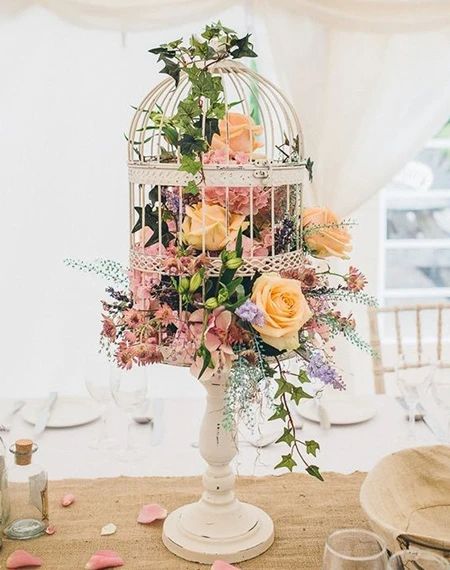 a vintage white cage placed on a stand with muted blooms and greenery is a chic idea for a vintage wedding