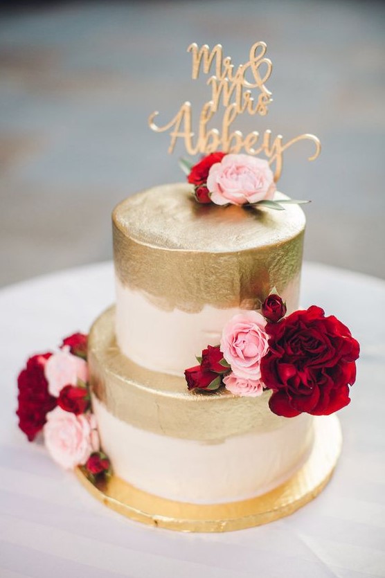 a wedding cake with gold leaf, pink and deep red blooms and a calligraphy gold topper for a glam wedding