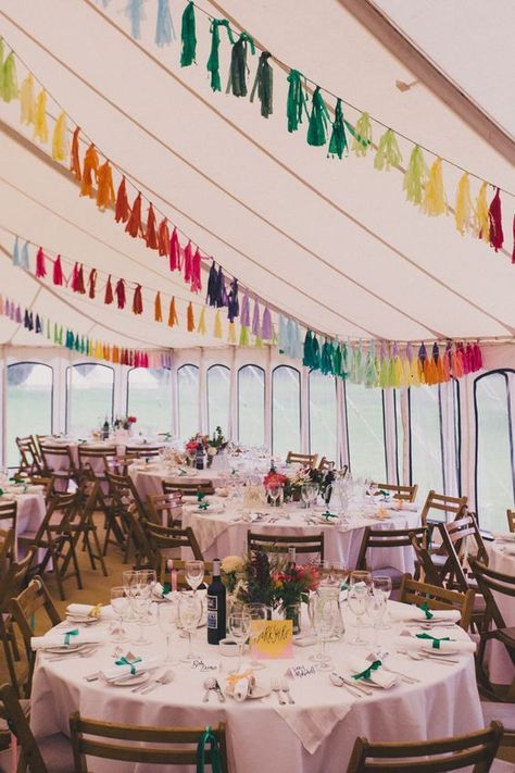a wedding reception space with bright blooms and greenery and colorful tassel garlands is a cool and lively space for a wedding