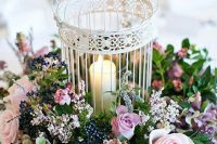 a whiet cage with a pillar candle and lush pink roses, berries and greenery for a garden wedding