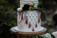 a white boho wedding cake with braids and macrame, with ombre tassels, fresh fruit and leaves is a lovely boho chic wedding idea