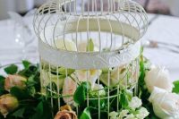 a white cage and greenery, blush and mauve roses is a lovely and lush wedding centerpiece