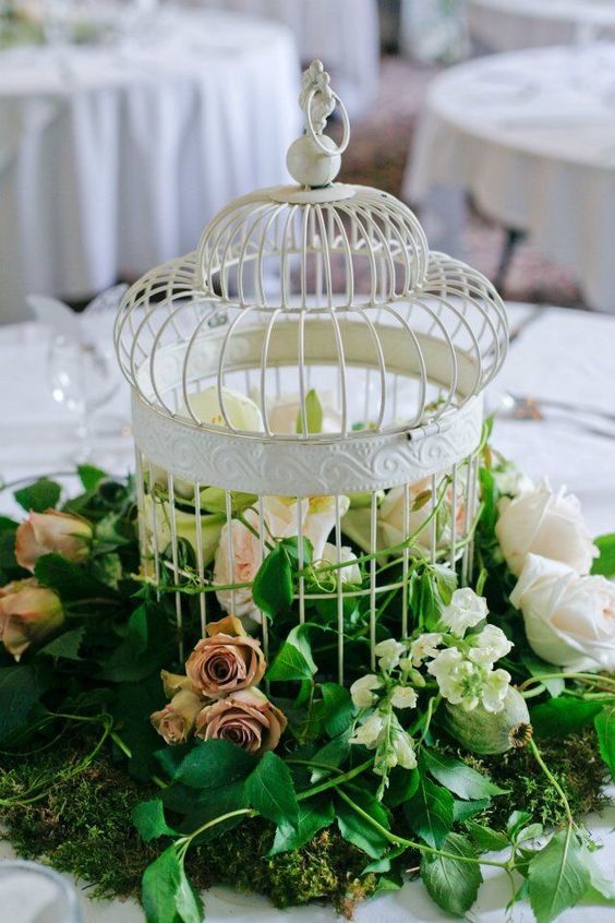 a white cage and greenery, blush and mauve roses is a lovely and lush wedding centerpiece