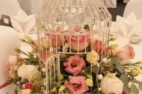 a white cage with white, pink and yellow blooms and greenery is a lovely wedding centerpiece idea