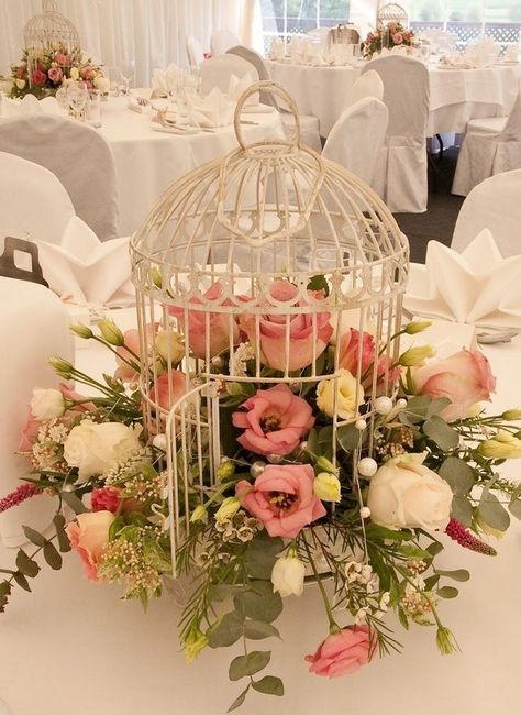 a white cage with white, pink and yellow blooms and greenery is a lovely wedding centerpiece idea
