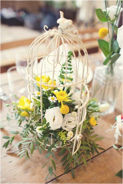 a white mini birdcage with greenery, white and yellow blooms is a chic and refined wedding centerpiece