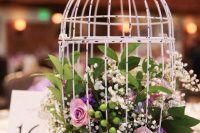 a white shabby chic cage with pink and purple roses, baby’s breath, greenery is a cool wedding centerpiece